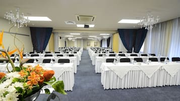 Une salle de conférence avec des rangées de tables, de chaises et des lustres.