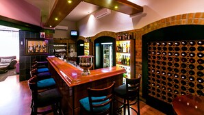 A bar area with a wooden bar, multiple stools, a wine rack, and a television in the background. - Cape Town Lodge Hotel (Cape Town)