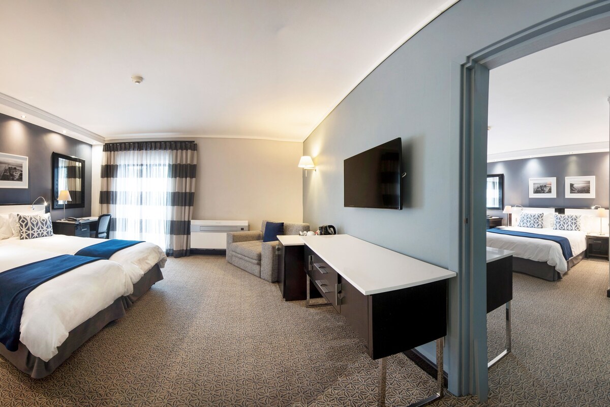 Habitación de hotel con dos camas, un escritorio, una silla, un televisor y un espejo grande.