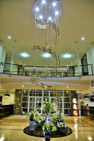 A lobby with a modern chandelier, a reception desk, and a staircase leading to an upper floor.