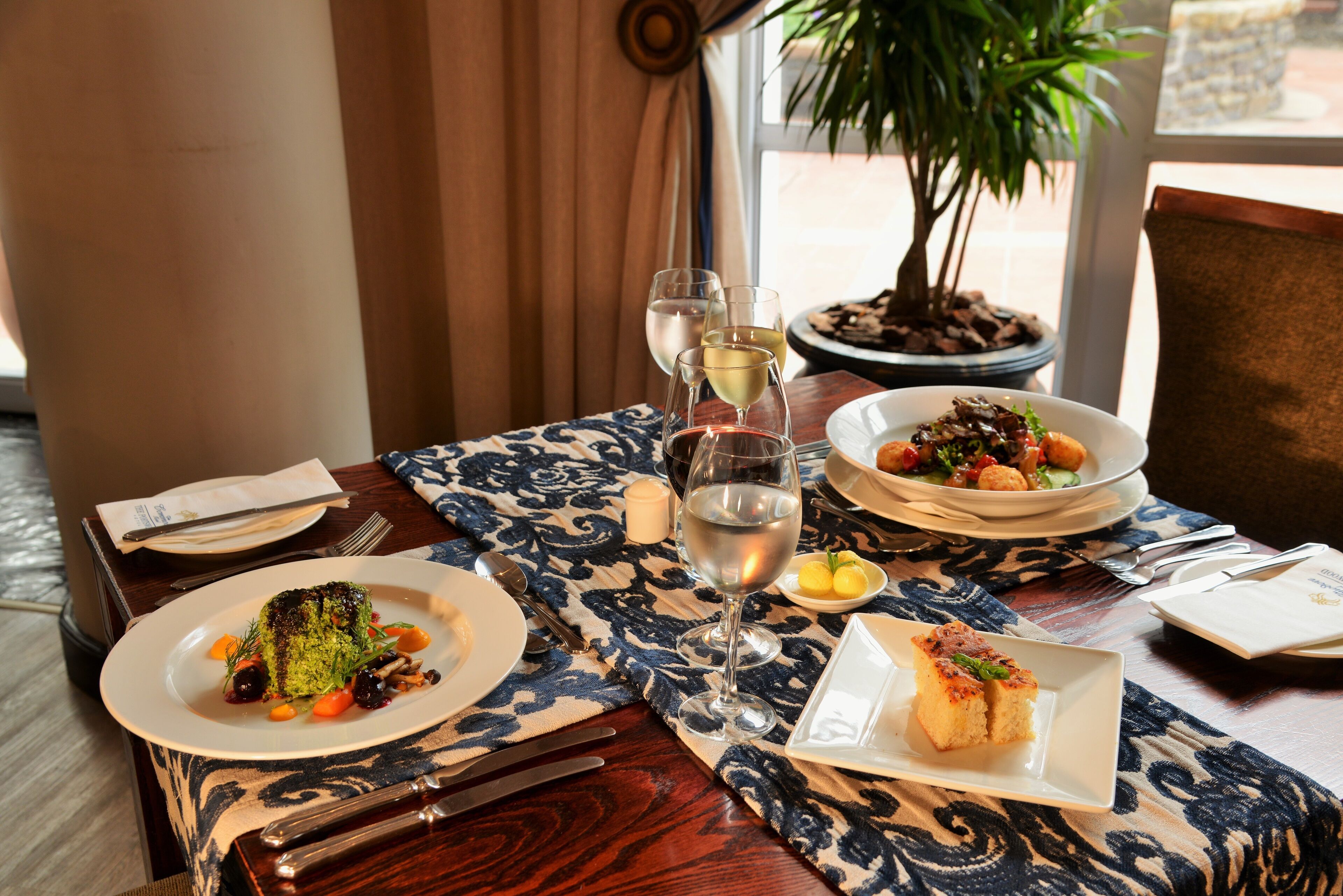 A dining table set with plates of food, wine glasses, and cutlery.