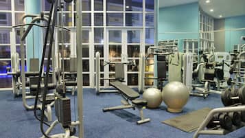 A gym with various exercise equipment, large windows, and a blue carpet.
