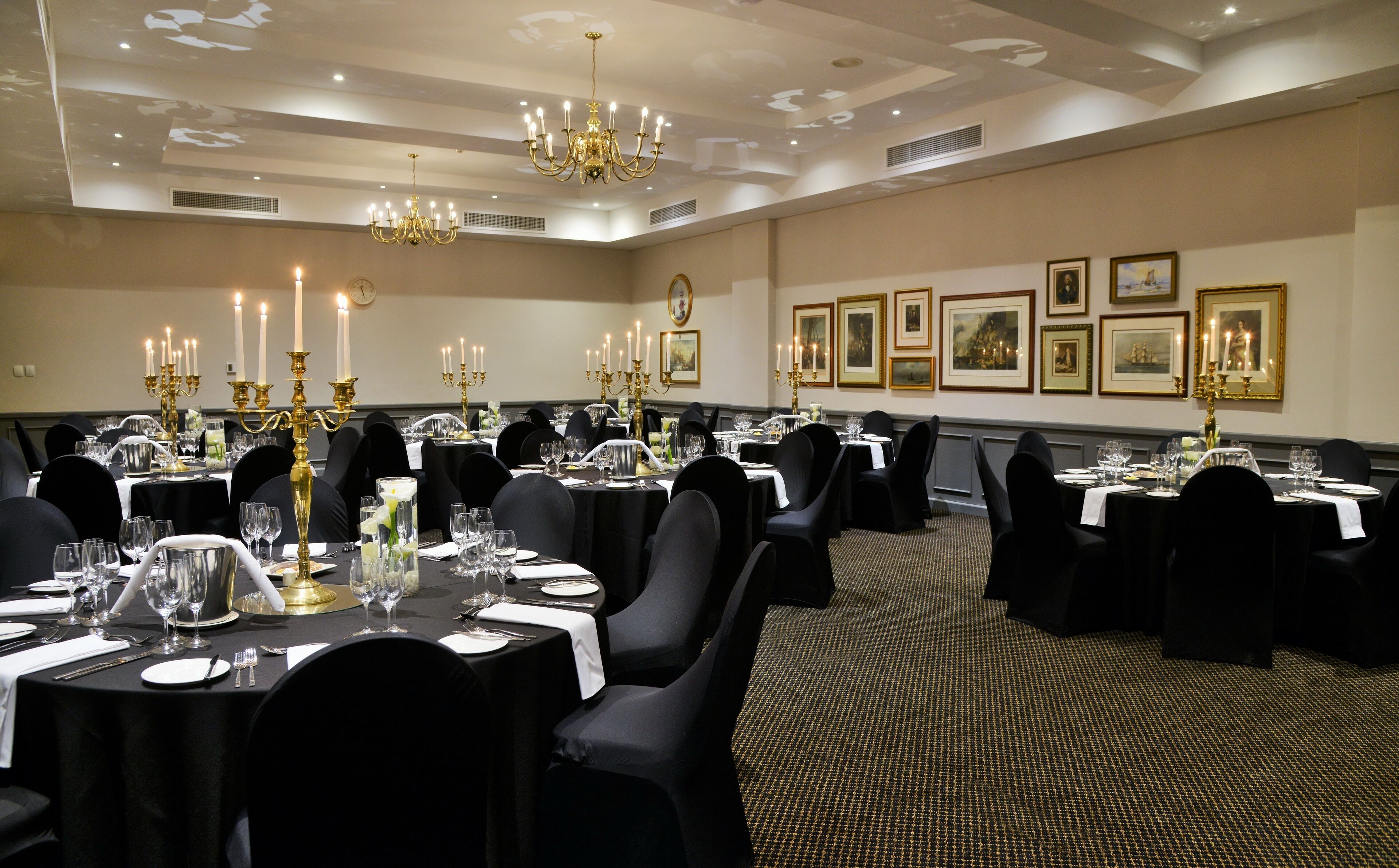 Une salle de banquet avec des tables rondes, des nappes noires et des chandeliers dorés.
