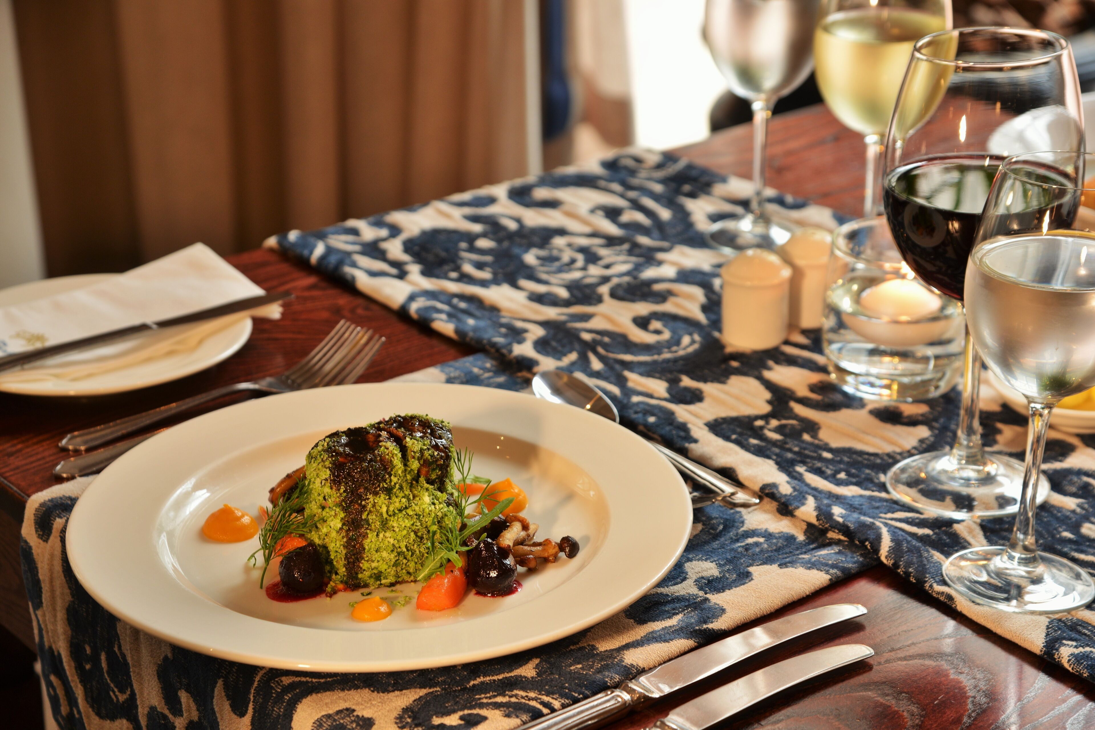 A dining table set with a plate of food, cutlery, glasses, and a candle.