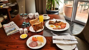 Una mesa de desayuno con diferentes alimentos, un periódico y vistas al patio exterior.