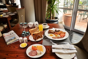 A breakfast table with various food items, a newspaper, and a view of the outdoor patio.