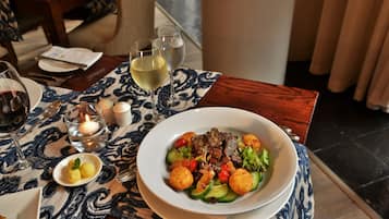 A dining table with a plate of food, two glasses of white wine, a candle, and a small bowl of lemon slices.