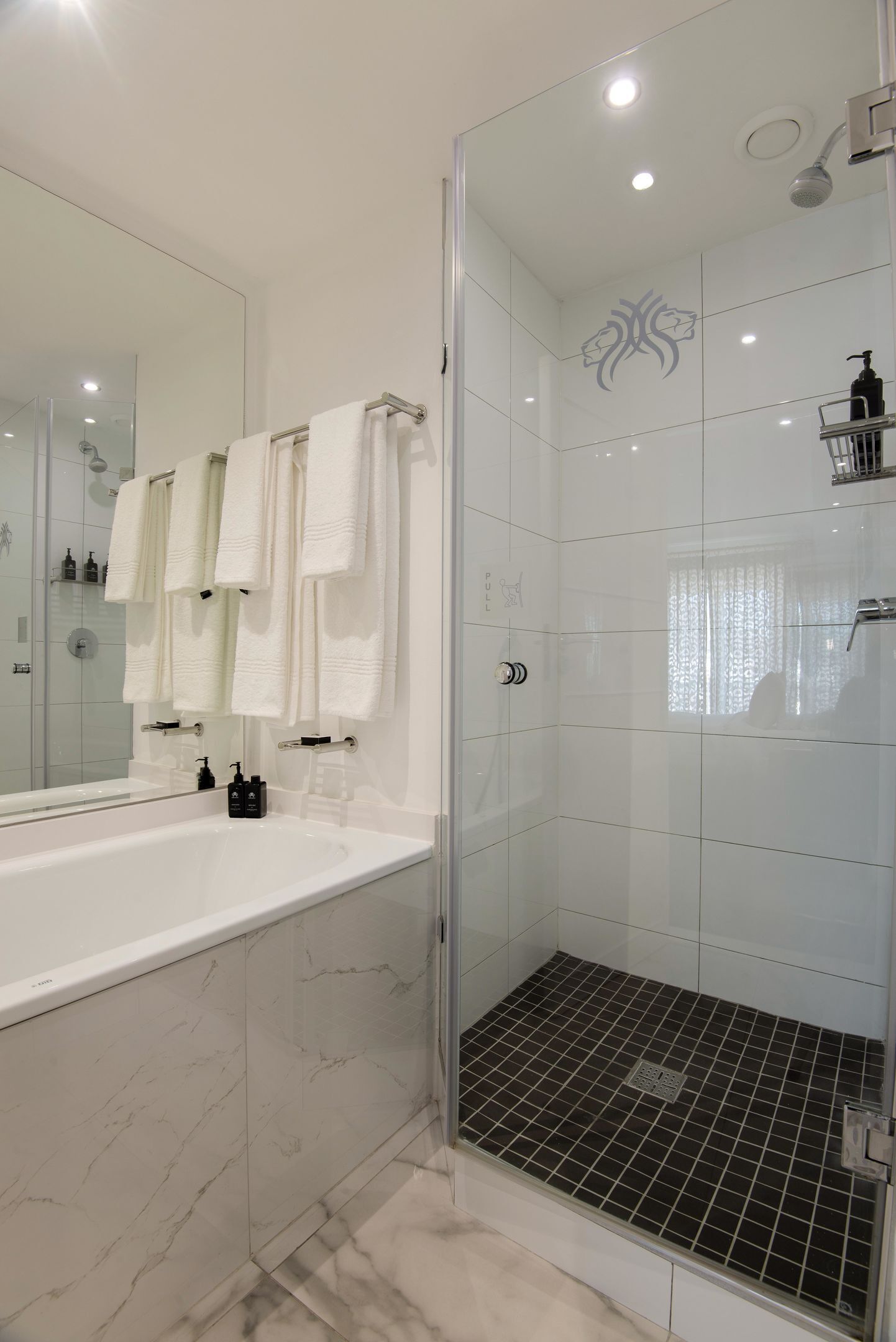 A modern bathroom with a glass-enclosed shower, a large mirror, and a white marble vanity.