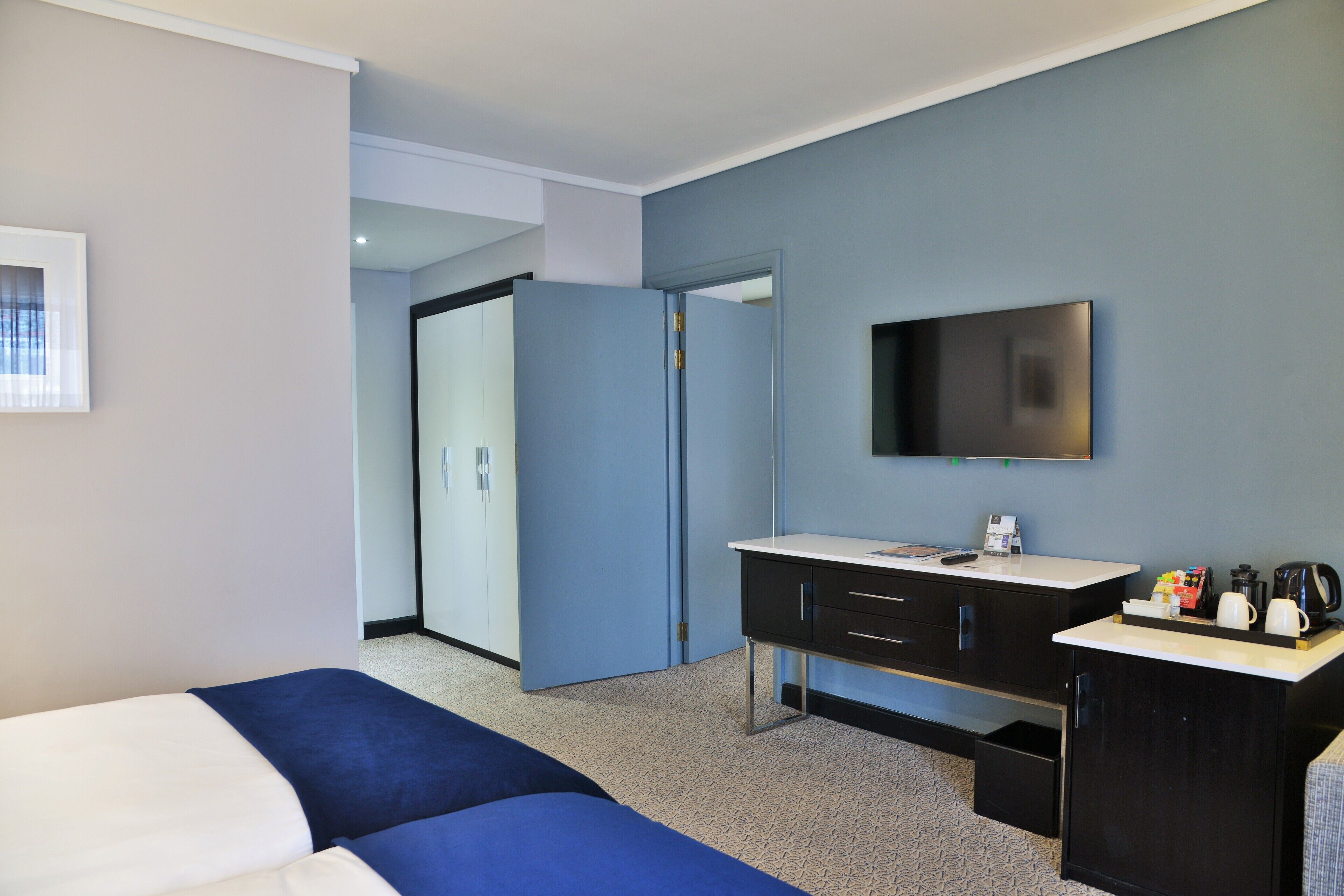 A hotel room with a bed, a desk with a flat-screen TV, a coffee maker, and a small kitchenette.
