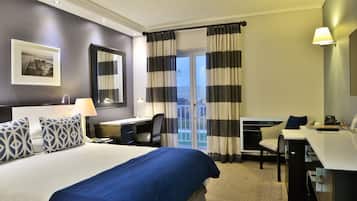 A hotel room with a large bed, a desk, a chair, a desk lamp, a telephone, and a window with curtains.