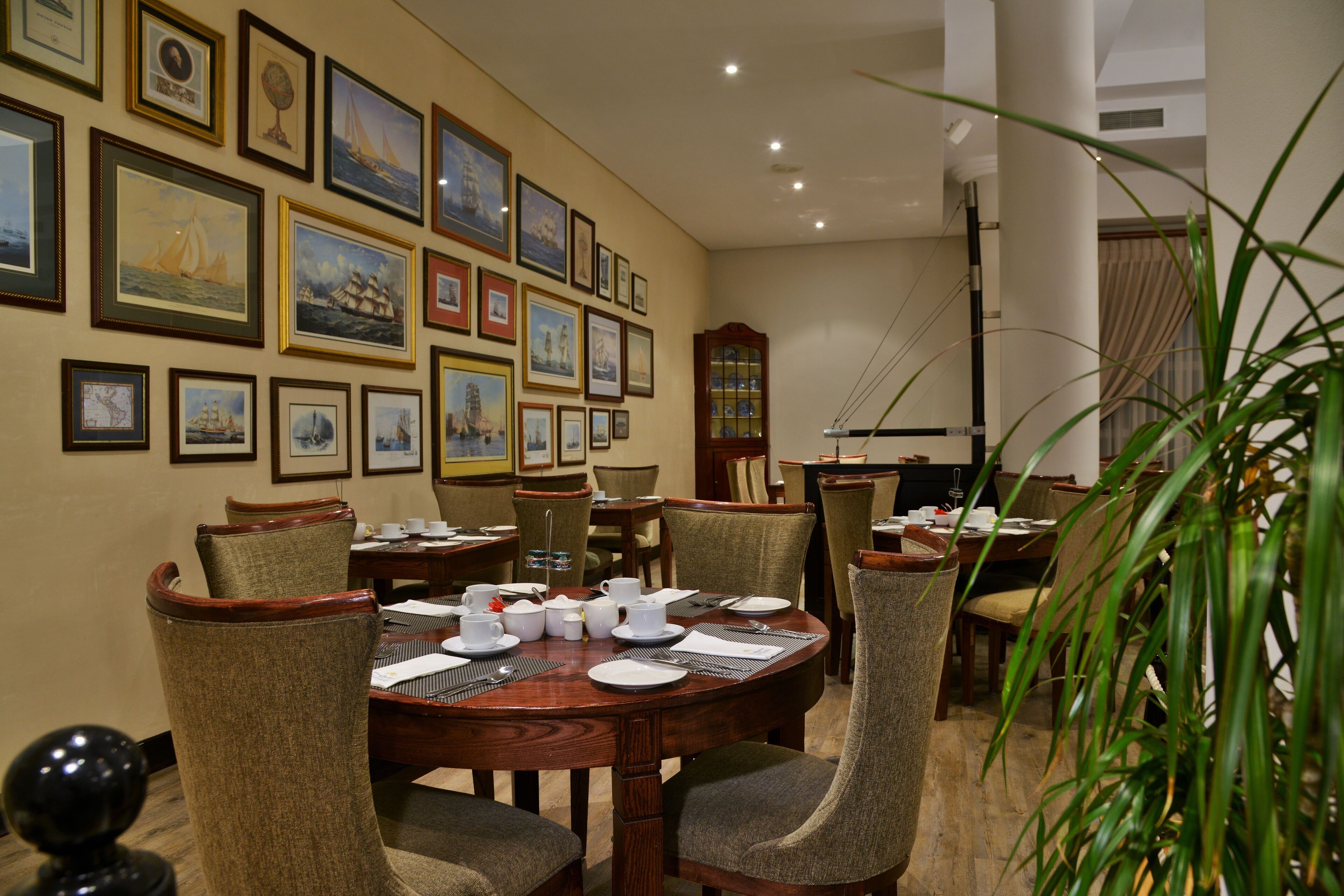 A dining area with a round wooden table, multiple chairs, and framed artwork on the walls.