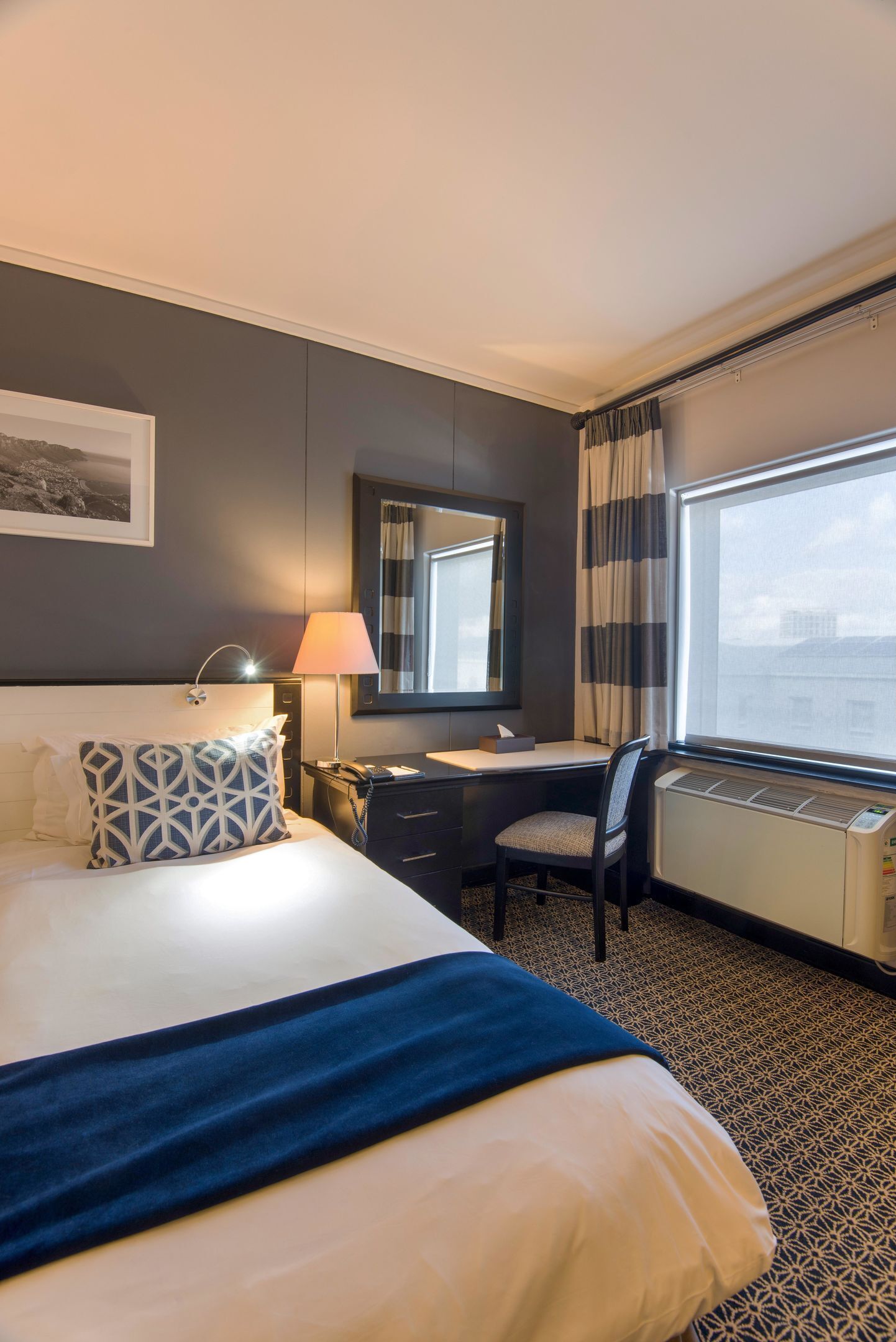 A hotel room with a bed, desk, chair, and a large window with curtains.