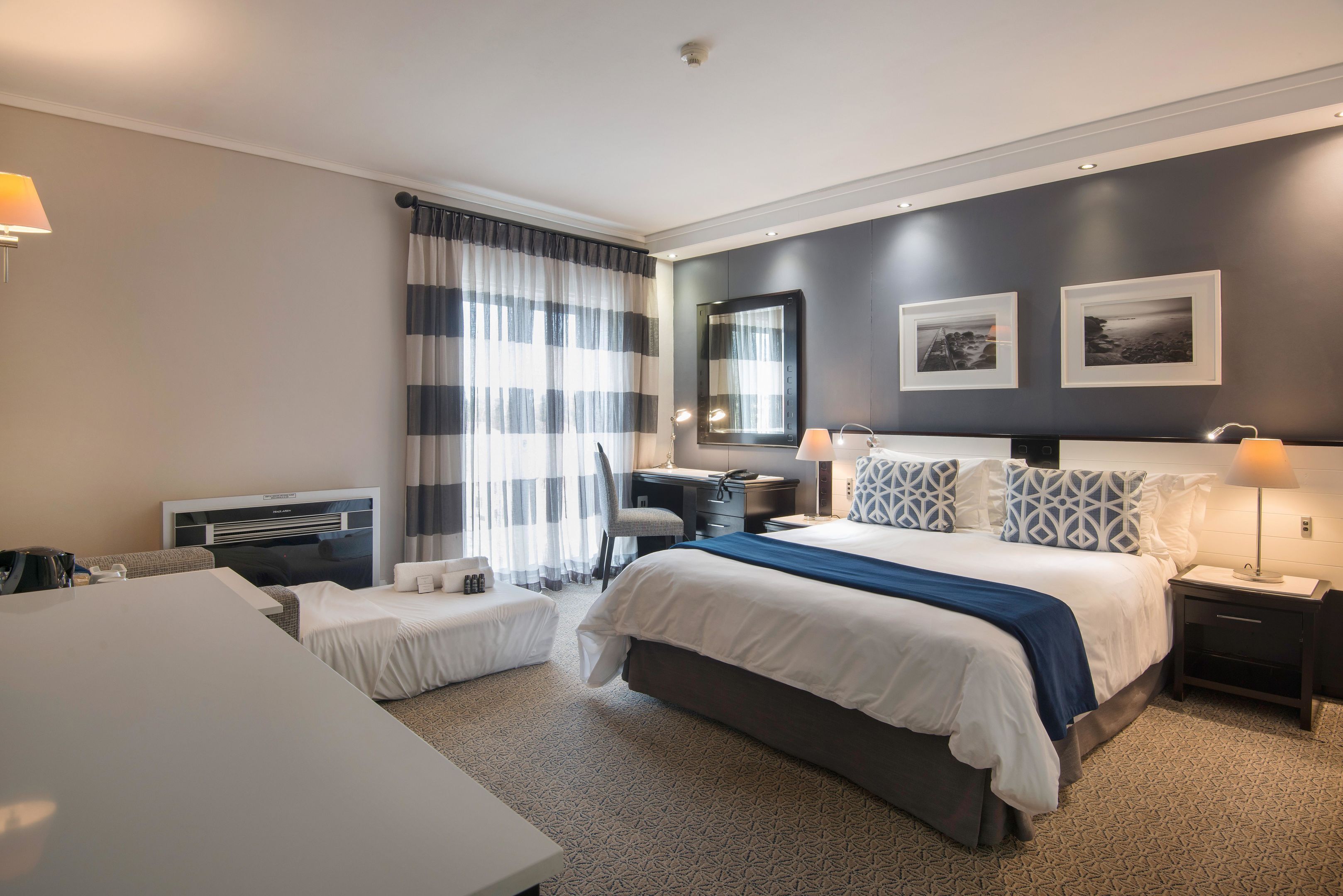 A hotel room with a large bed, a desk, a chair, and a small table.