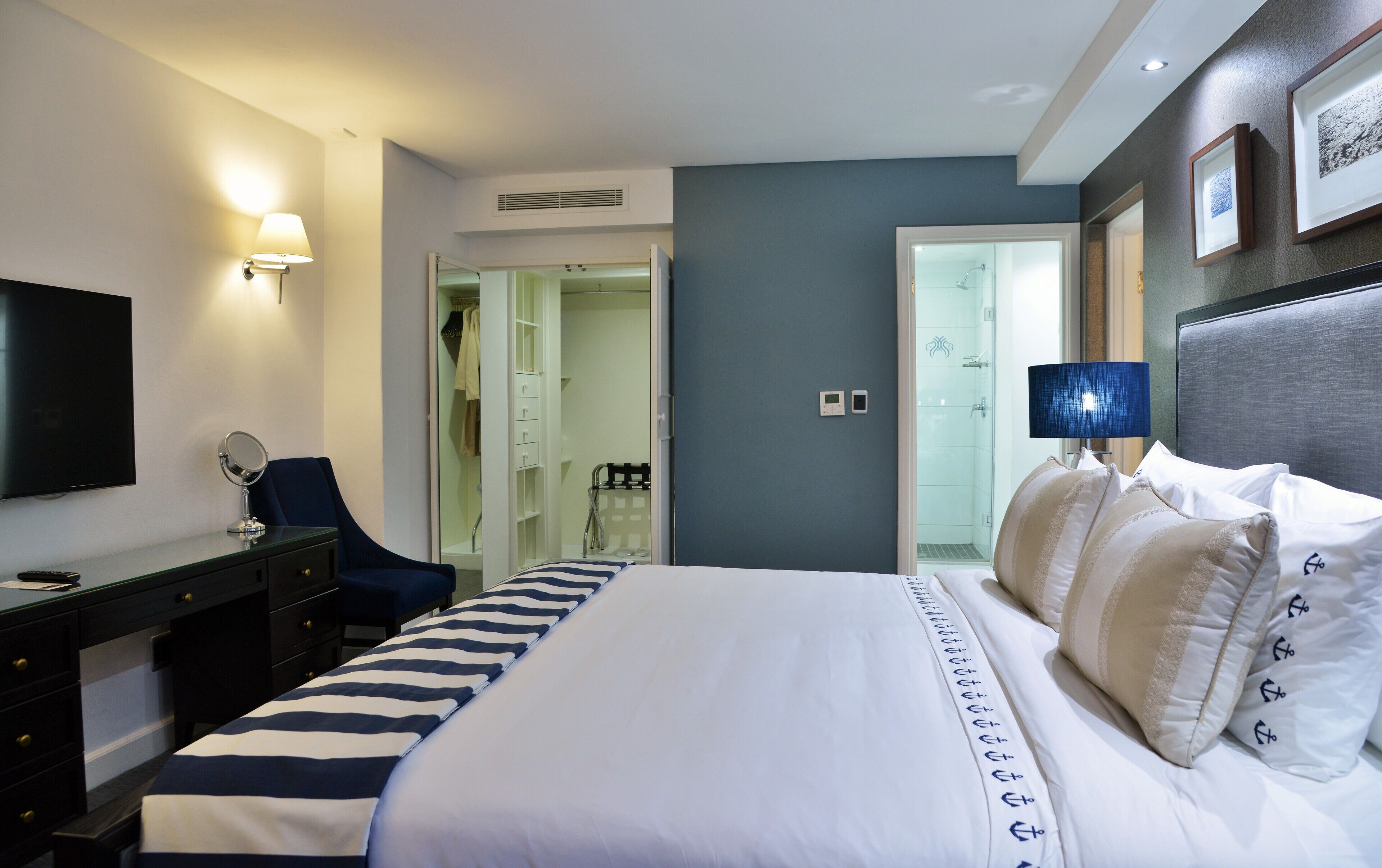 A hotel room with a bed, a desk, a chair, a TV, and a bathroom visible through an open door.