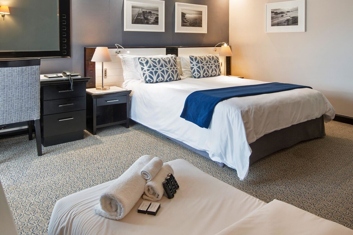 Habitación de hotel con cama, mesitas de noche, escritorio y una silla.