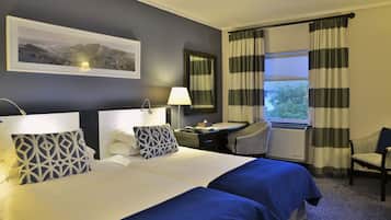 A hotel room with two beds, a desk, a chair, a lamp, a mirror, and a window with curtains.