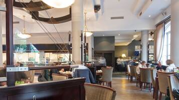 A spacious restaurant with high ceilings, modern lighting, and a central dining area with wooden tables and chairs.