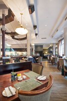 A spacious restaurant with high ceilings, modern lighting, and a central dining area with wooden tables and chairs.