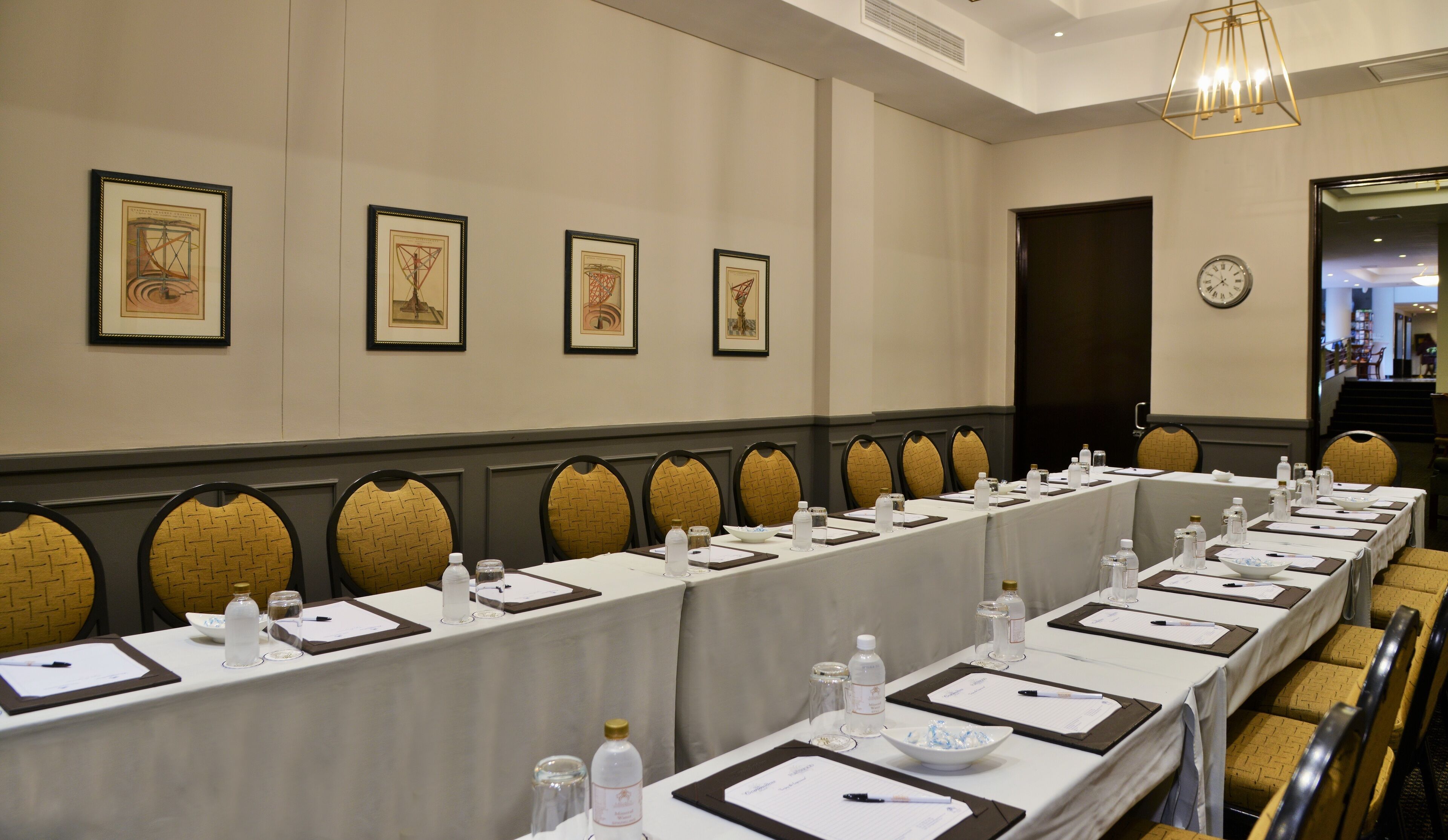 A conference room with long tables, chairs, and framed artwork on the wall.