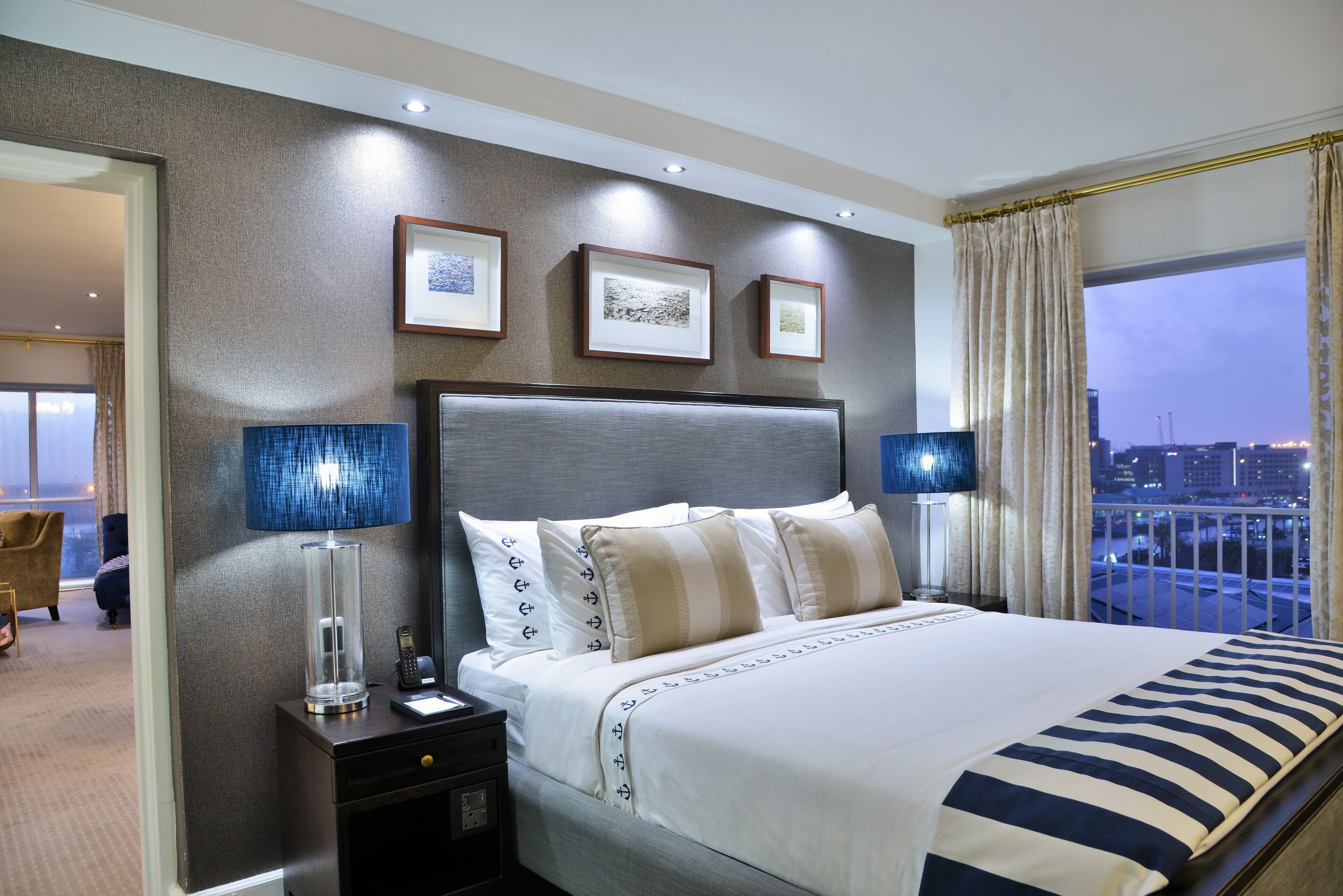 A hotel room with a large bed, two bedside lamps, a nightstand, and framed pictures on the wall.