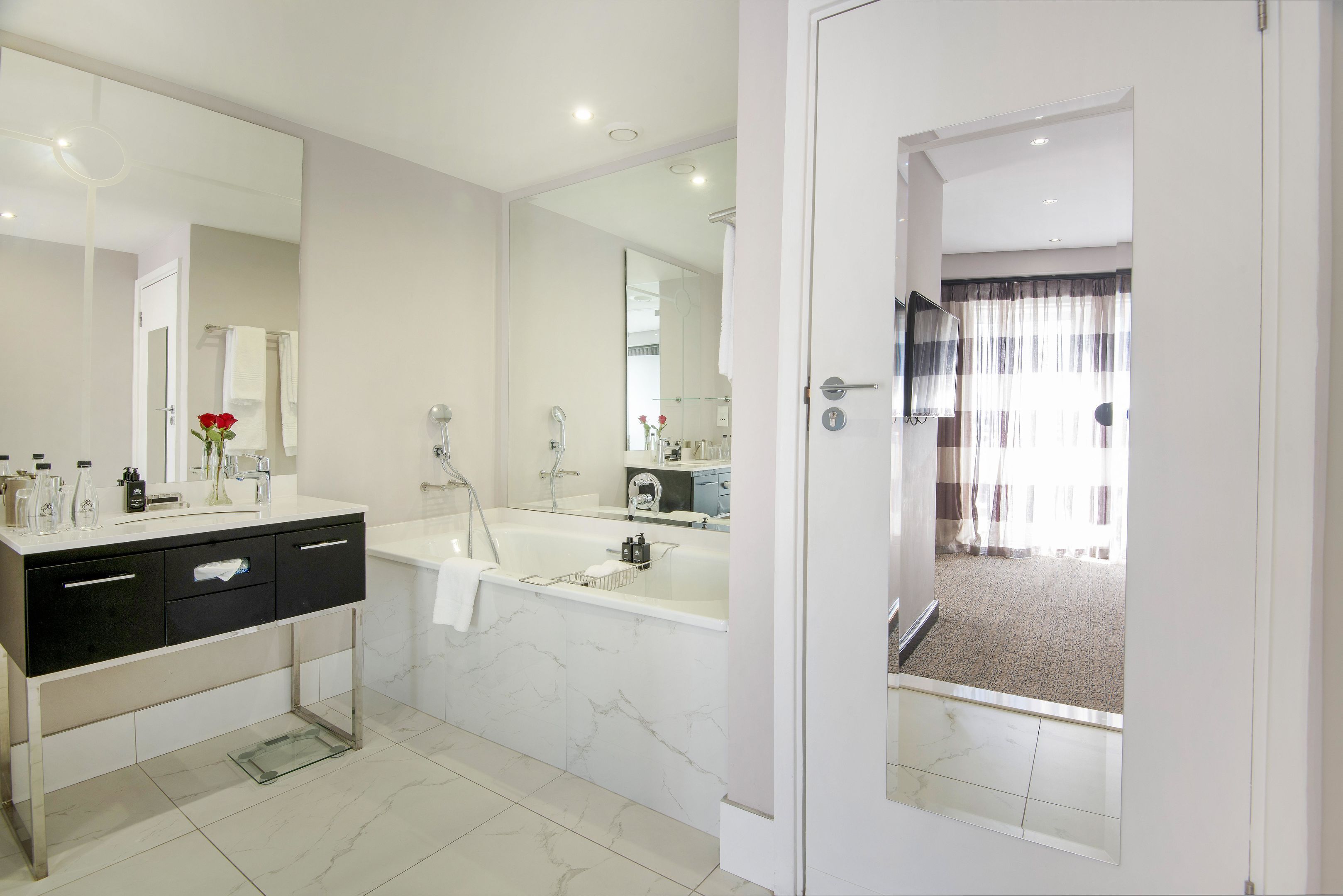 A modern bathroom with a large mirror, a black vanity, a bathtub, and a shower.