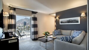 Una habitación de hotel moderna con un sofá gris, una zona de café, vistas a la ciudad y un balcón con cortinas a rayas.
