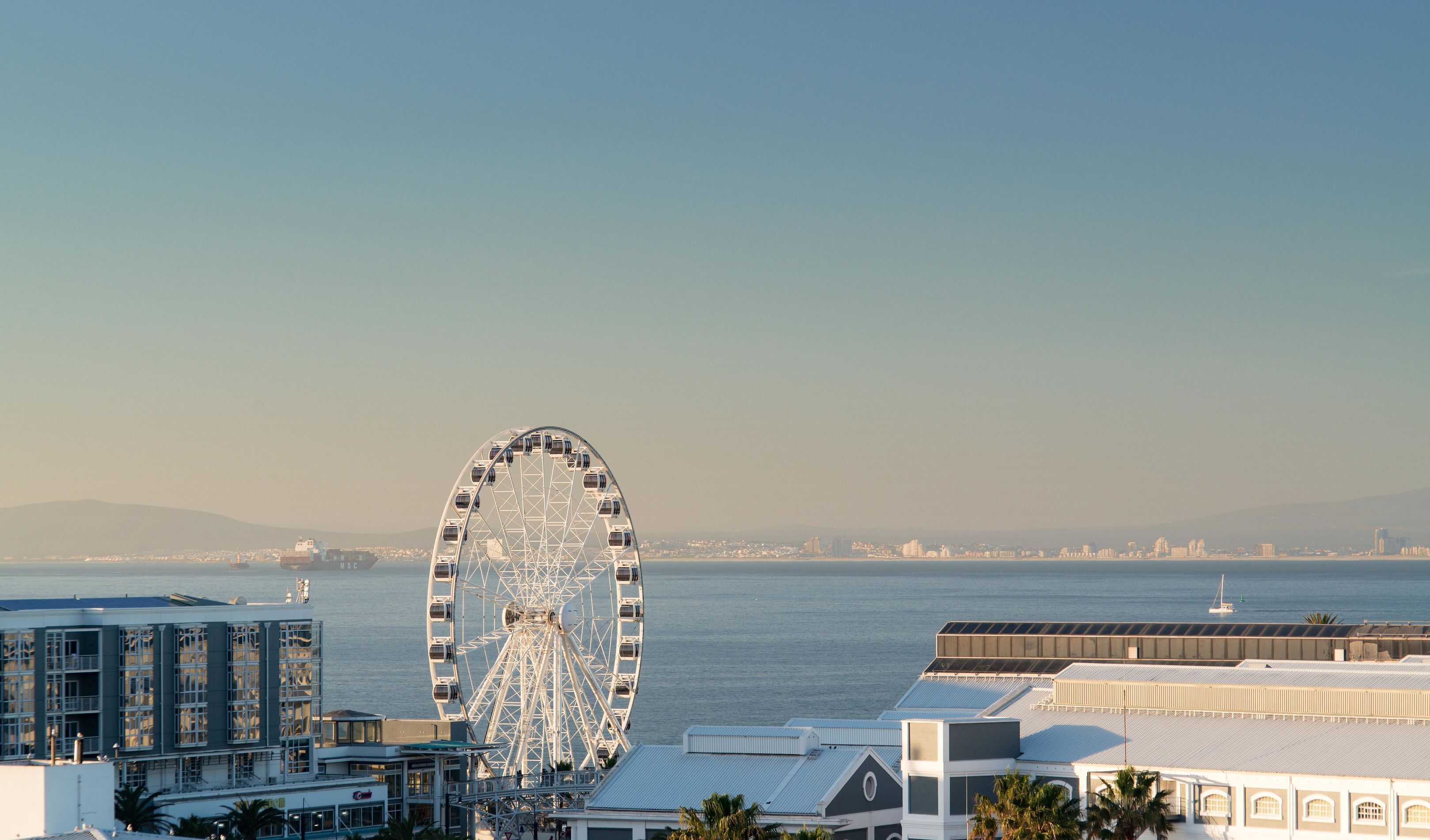 A waterfront view with a prominent Ferris wheel, modern buildings, and a clear sky.