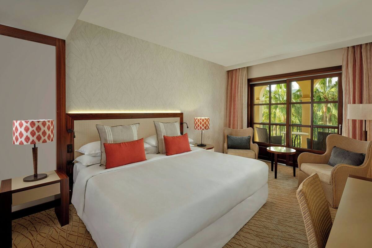 A hotel room with a large bed, two bedside tables, a small round table, and a sofa.