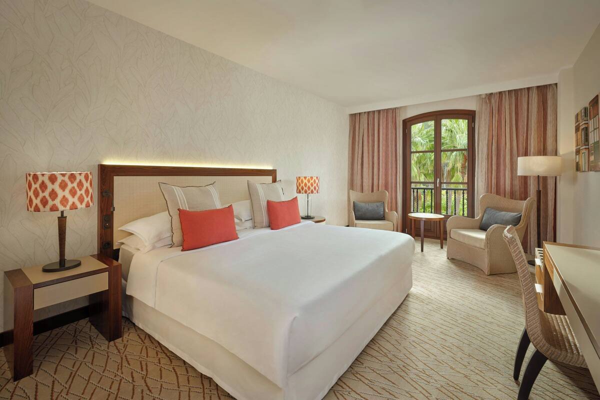 A hotel room with a large bed, two chairs, a desk, and a window with curtains.