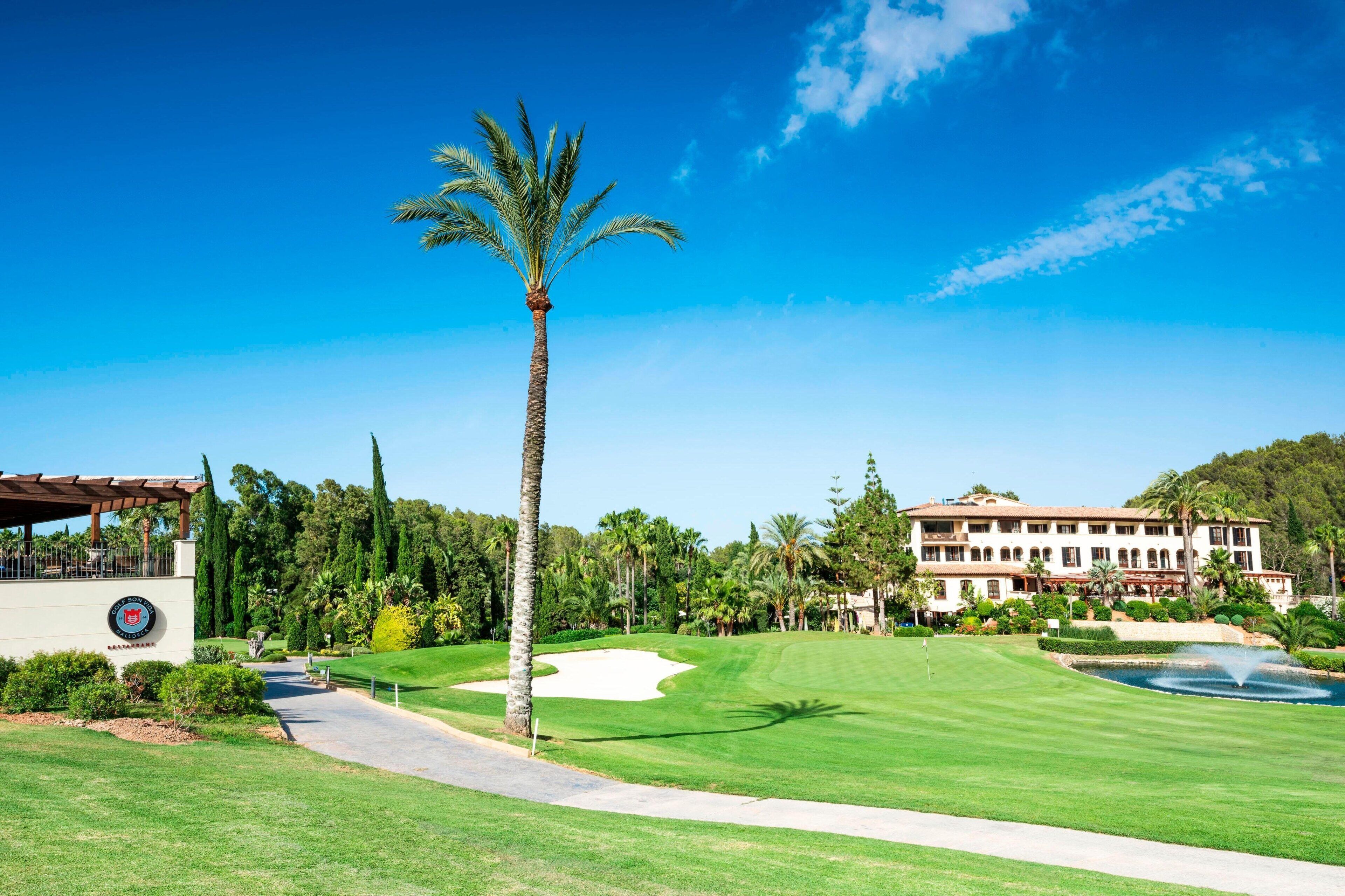 Ein Golfplatz mit Clubhaus, Palmen und einem großen Gebäude mit Garten im Hintergrund.