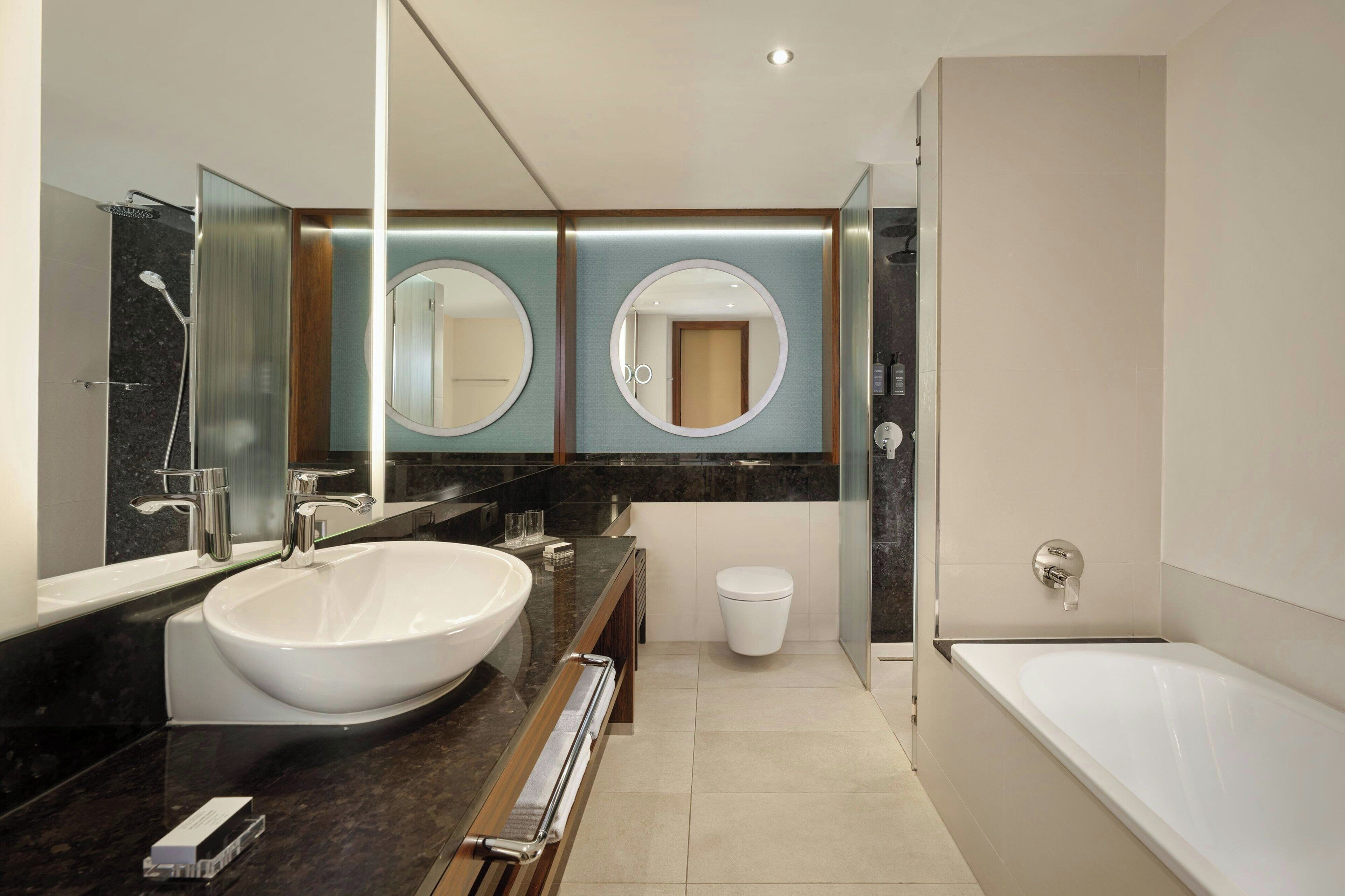 Ein modernes Badezimmer mit einem großen Waschbecken, zwei runden Spiegeln, einer Toilette und einer Badewanne.