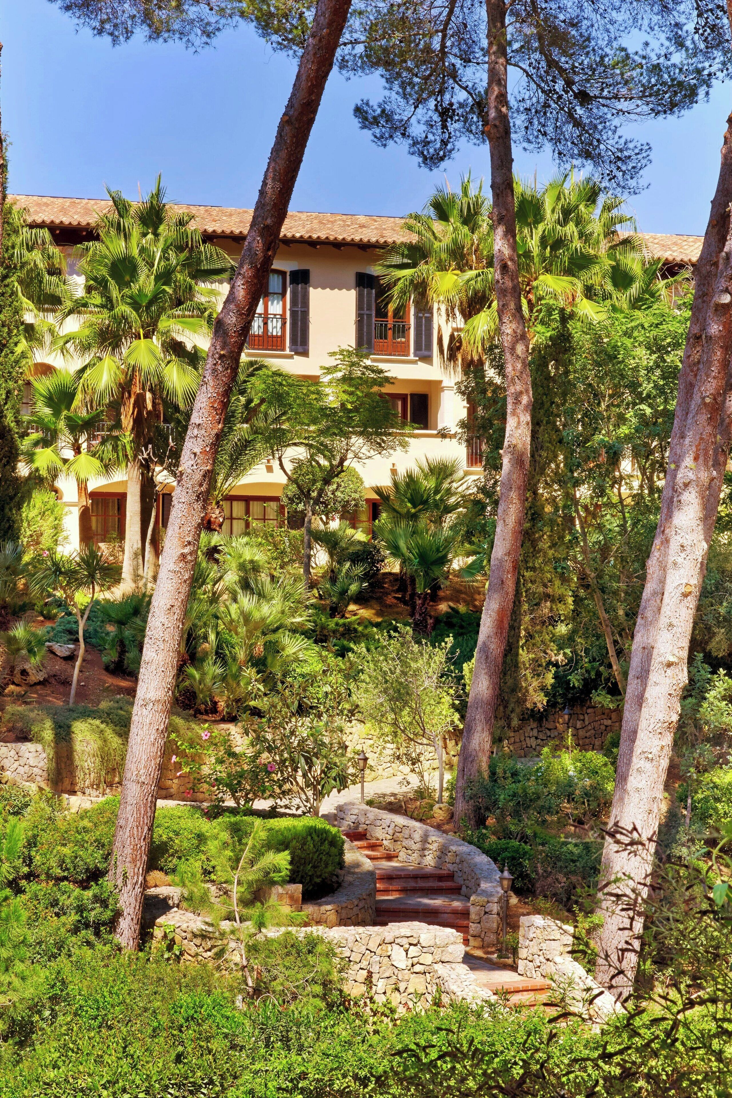 A resort with a stone pathway leading to a building with a tiled roof, surrounded by lush greenery and palm trees.