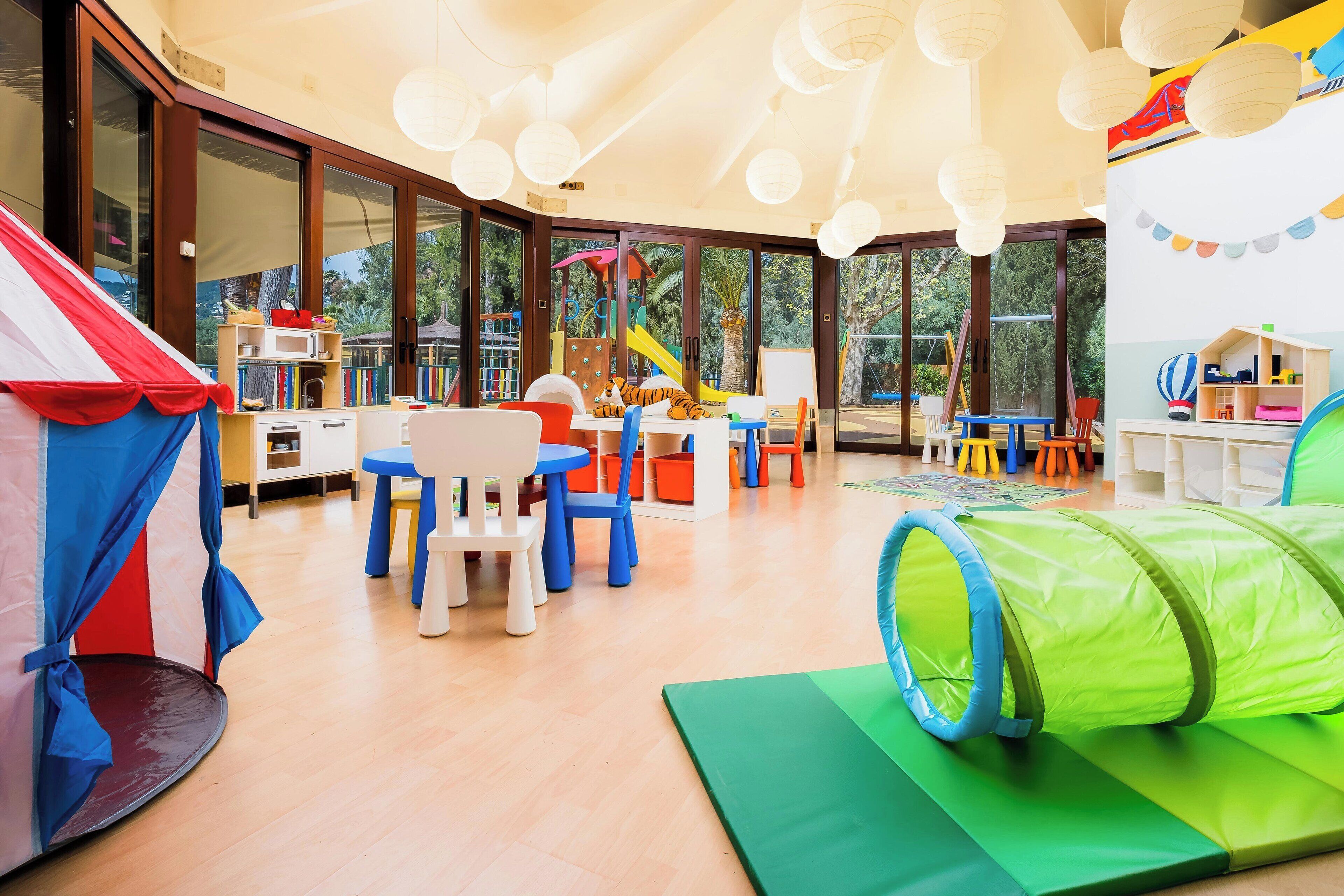 A spacious indoor play area with a large window, a play tent, and a green tunnel.