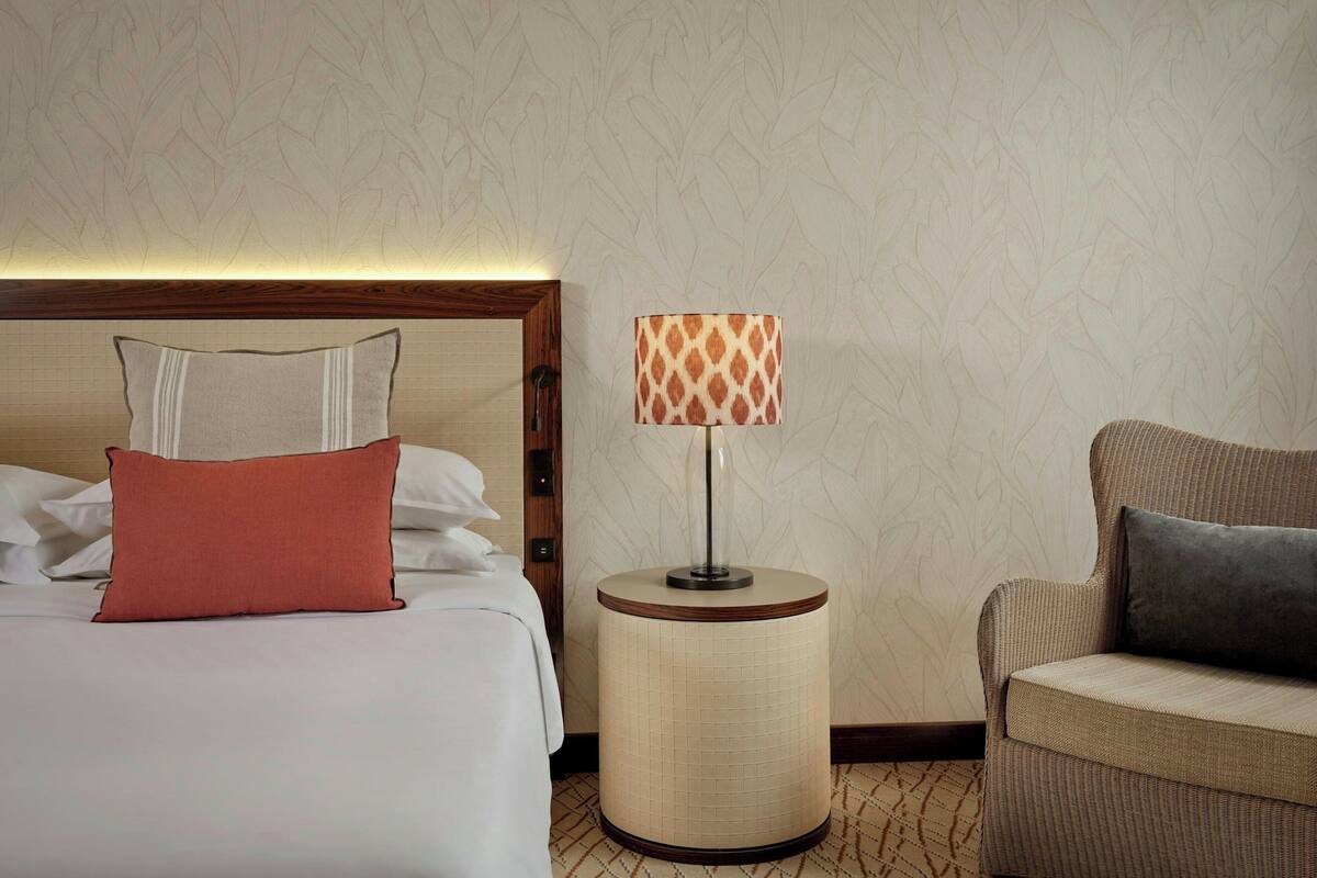 A hotel room with a bed, a round side table with a lamp, and a sofa.