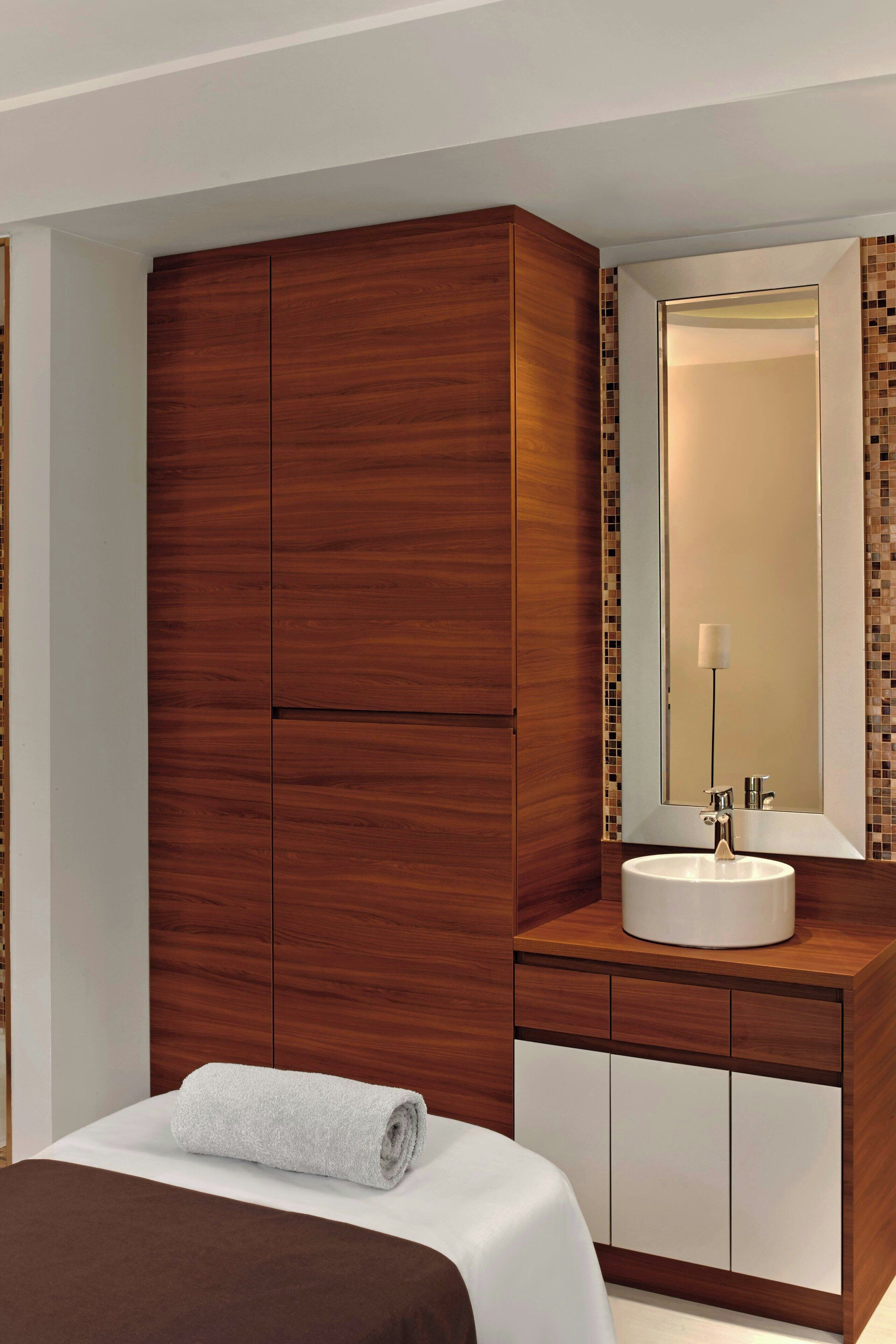 A hotel room with a large wooden wardrobe, a white sink, and a mirror above it.