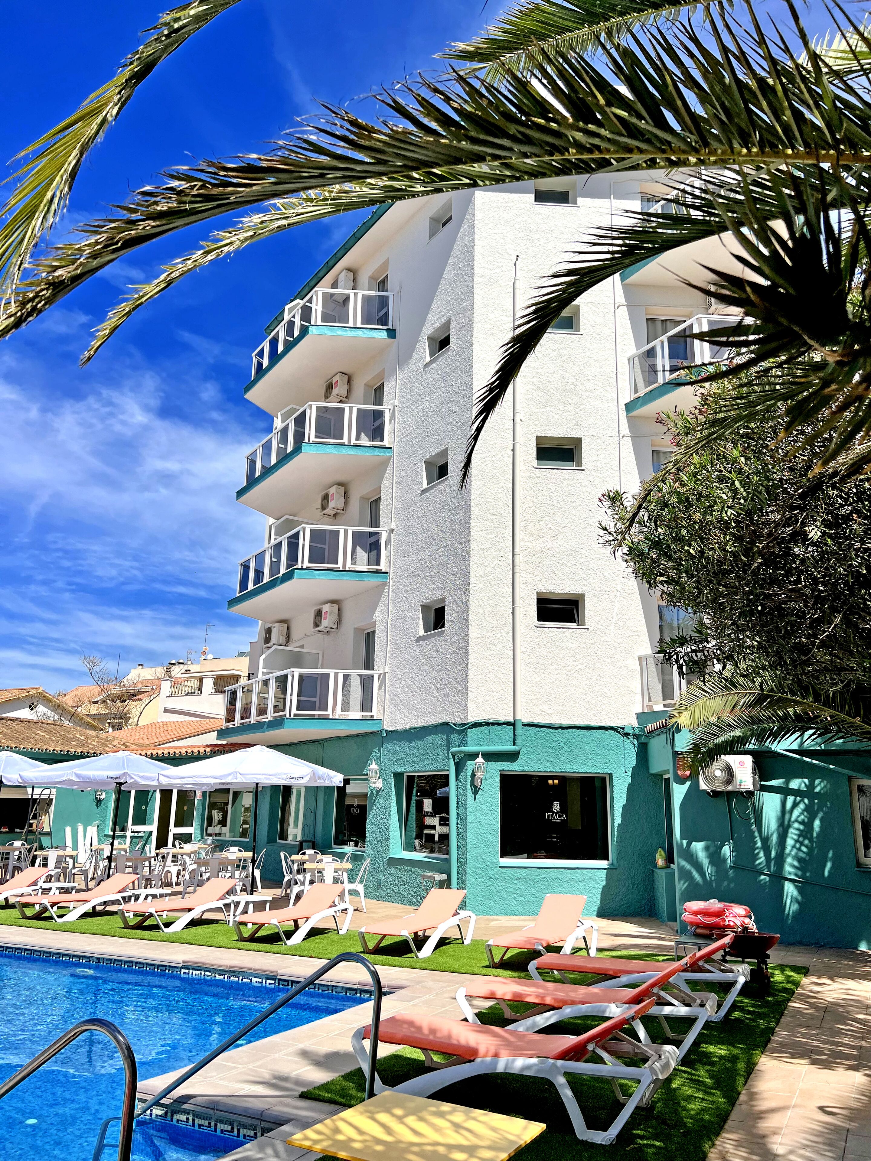 A multi-story hotel with a pool area, including lounge chairs and umbrellas.
