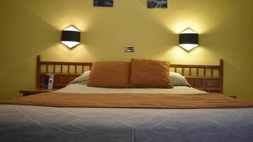 A hotel room with a bed, two wall-mounted light fixtures, and a small bedside table with a remote control.
