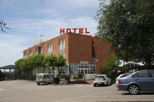 Un hotel con un letrero rojo llamativo, un estacionamiento con varios coches y un edificio de fachada de ladrillo.
