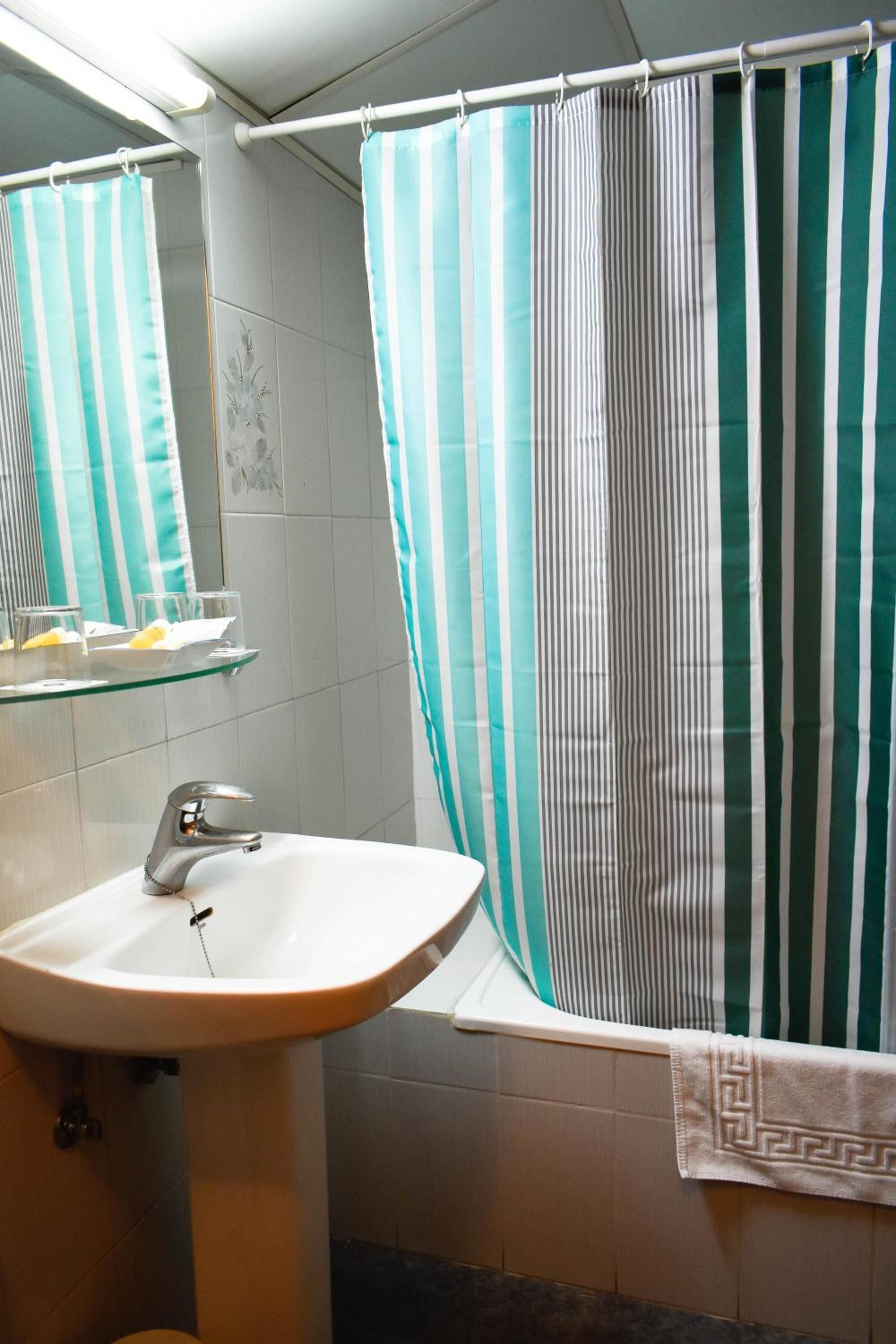 Een badkamer met een wit wastafel, een glazen plank, een gestreept douchegordijn en een handdoekrek.