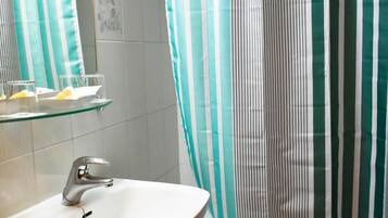 Un baño con un lavamanos blanco, un estante de vidrio, una cortina de ducha a rayas y un perchero.