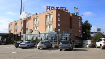 Un hotel con un cartel llamativo que dice 'HOTEL', un cartel de 'CAFETERIA' y un estacionamiento con varios coches.