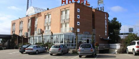 A hotel with a prominent 'HOTEL' sign, a 'CAFETERIA' sign, and a parking lot with several cars.