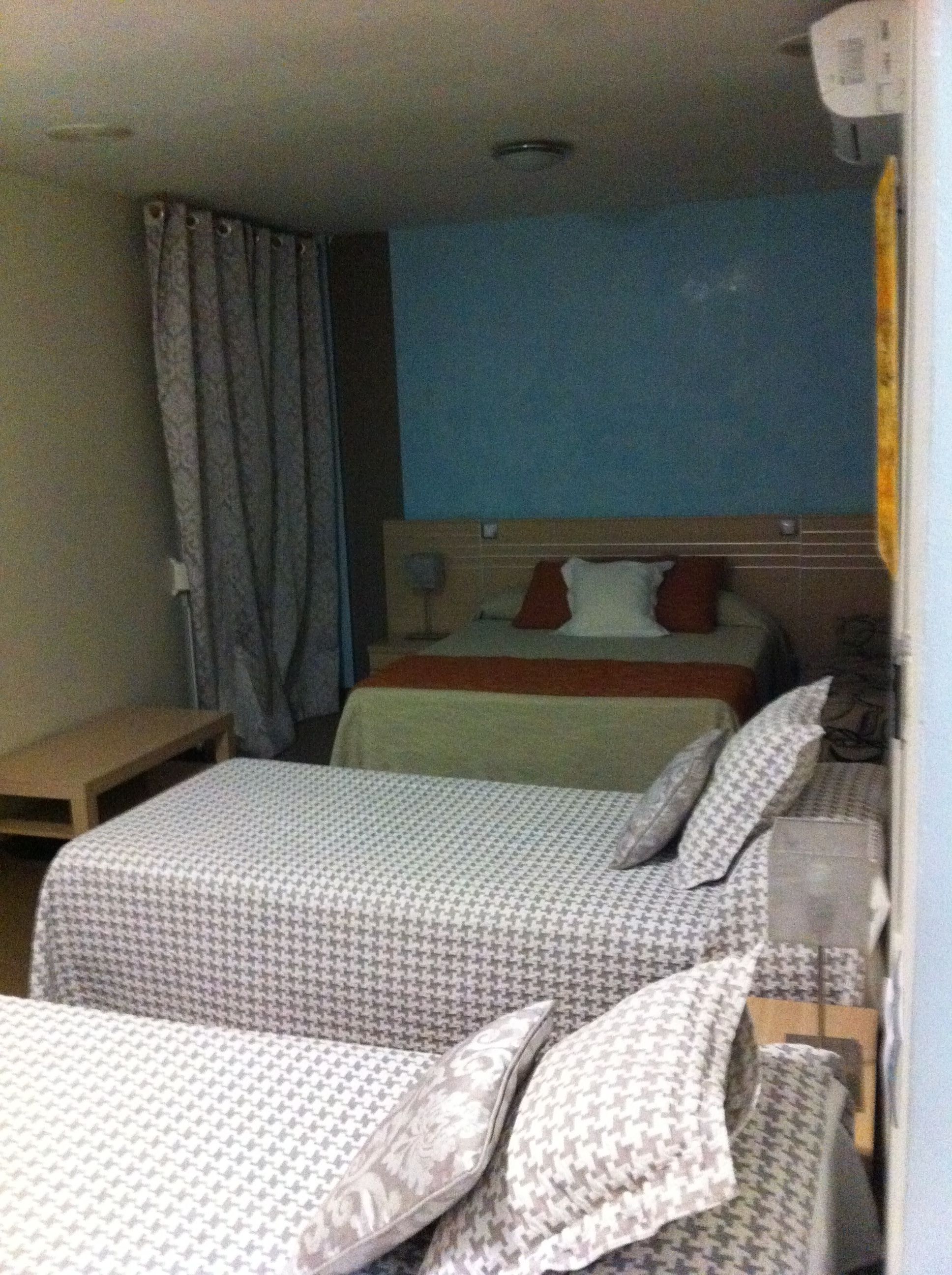 A hotel room with two beds, a nightstand, a desk, and a window with curtains.