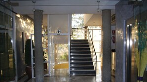 Un pasillo con suelo de mármol, una escalera, columnas grandes y un puerta de vidrio que da al exterior.