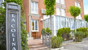 Entrada de un hotel con un letrero que dice "HOTEL LACOLINA", escalones que conducen a la puerta y un área de estacionamiento al frente.