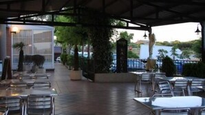 Un patio al aire libre con mesas y sillas, una zona de estar cubierta y vistas a la calle y la vegetación.