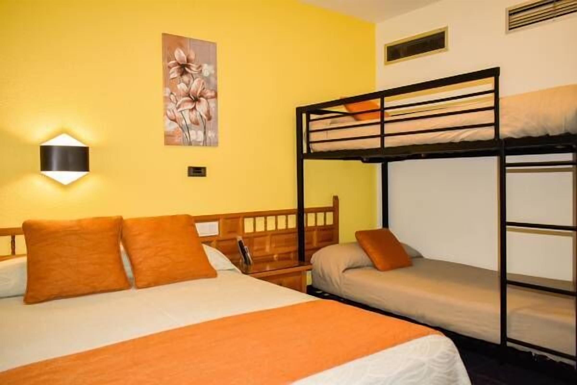 A hotel room with a bunk bed, a single bed, and a wall-mounted light fixture.