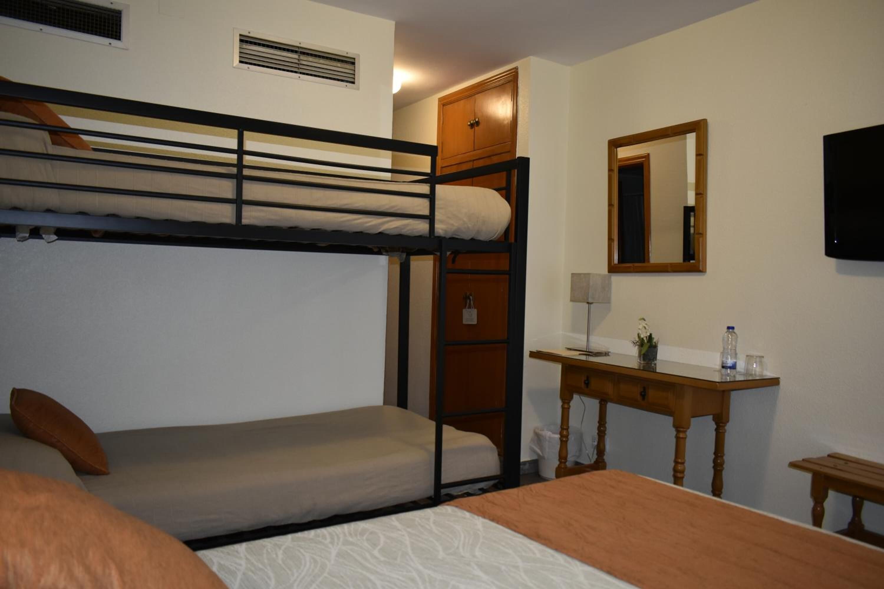 Een slaapkamer met een stapelbed, bureau, spiegel en een televisie.