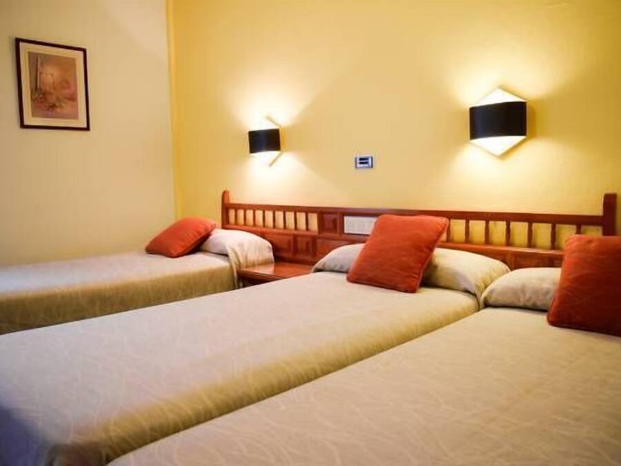 A hotel room with two single beds, each with a wooden headboard, and two wall-mounted night lights.