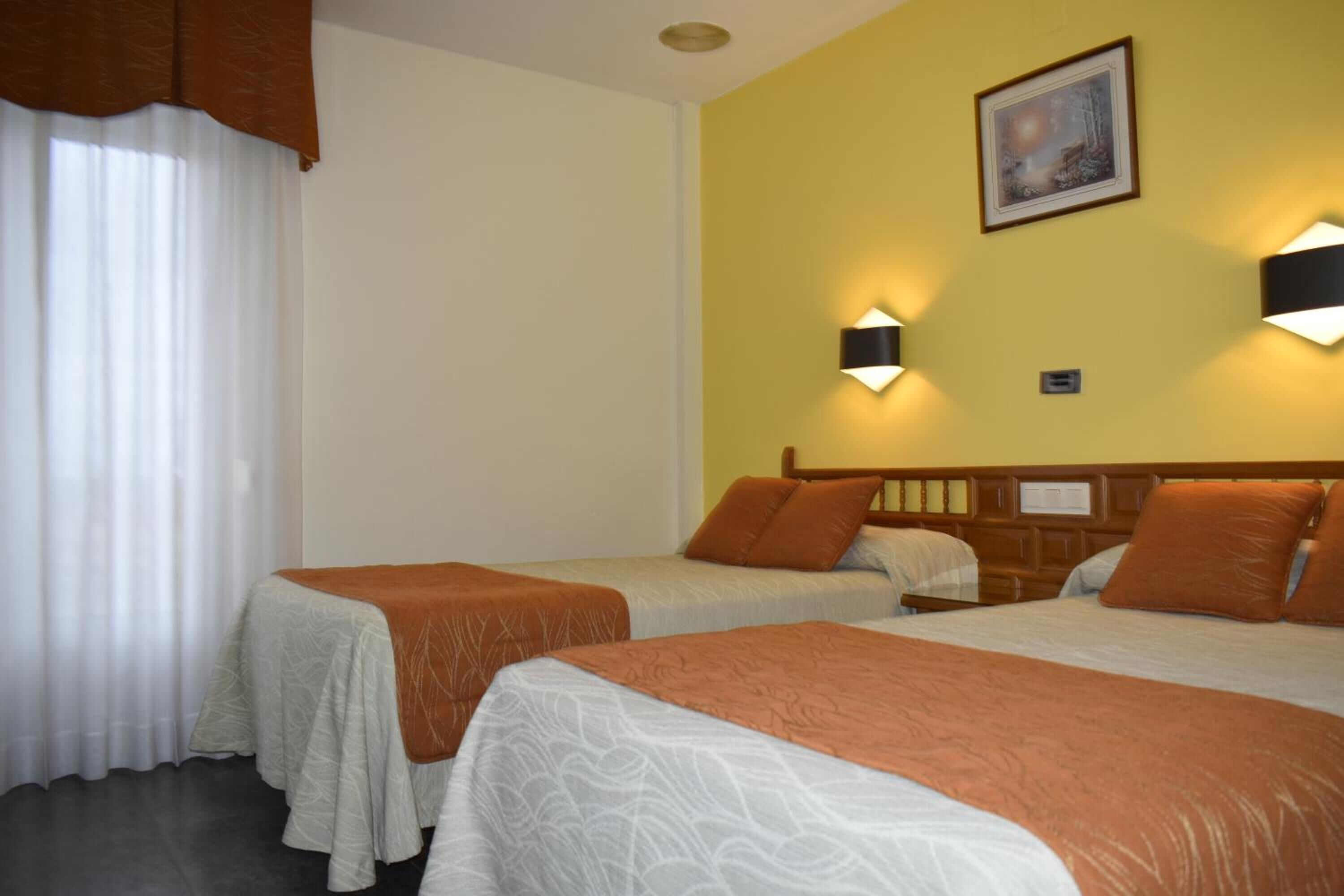 Habitació d'hotel amb dos llits, una paret groga i dues làmpades penjades a la paret.